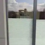 Miniaturka - Jasne plisy okienne sznurkowe w ciemnej ramie widziane od tarasu, montażysta osłon u klienta w Kobyłce.