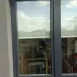 Miniaturka - Jasne plisy okienne podciągnięte wysoko w ciemnej ramie, widoczne narzędzia montażowe u klienta w Kobyłce.