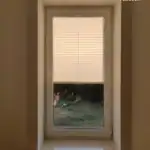 Miniaturka - Jasna plisa okienna opuszczona od góry do dwóch trzecich wysokości szyby w głębokiej wnęce z marmurowym parapetem.