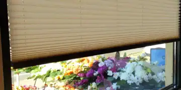 Jasne plisy okienne zamontowane w witrynie salonu usługowego w Warszawie, widok na ekspozycję kwiatową przez szybę.